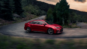 A red 2023 Toyota Corolla Hybrid compact sedan model driving on a curving forest road