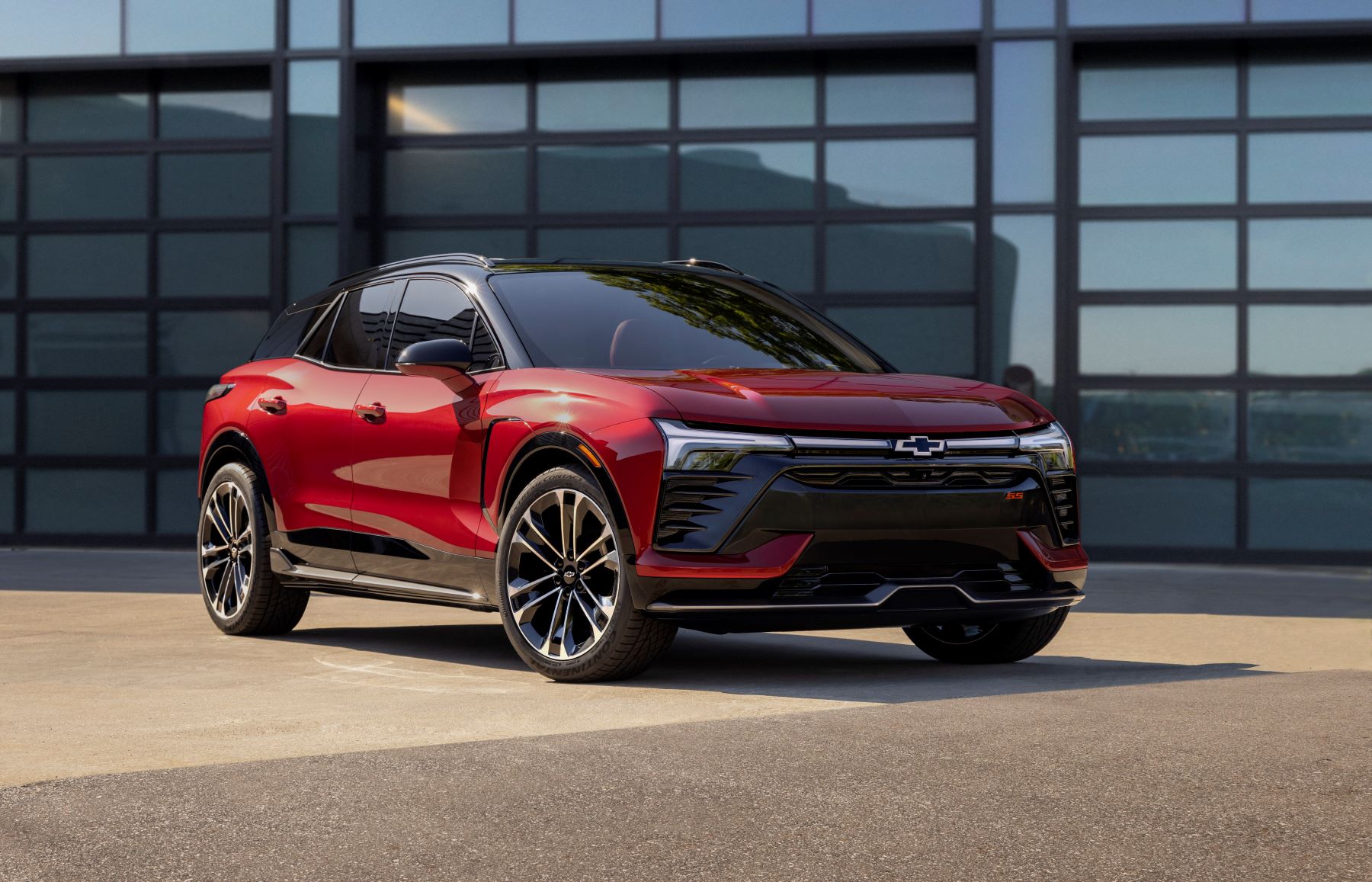 A red 2024 Chevrolet Chevy Blazer EV all-electric compact SUV model parked outside a reflective garage door