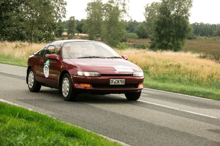 A red burgundy Toyota Sera hatchback coupe model driving on a country road