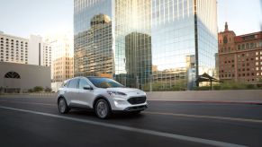 A white 2022 Ford Escape compact SUV driving past a reflective skyscraper