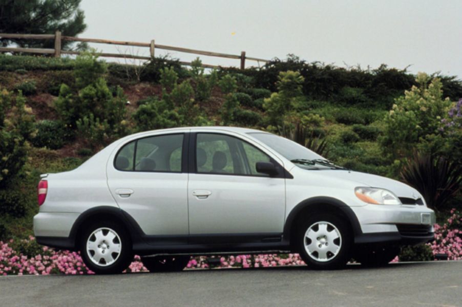 A light-gray 2000-2002 first-generation Toyota Echo sedan parked by pink flowers