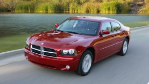 Red 2010 Dodge charger driving along a remote road, a pond visible in the background.