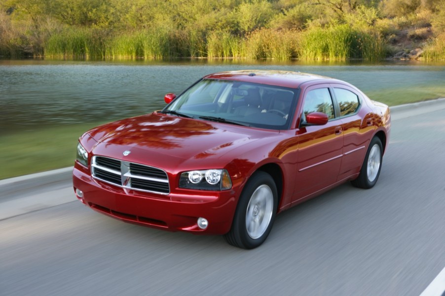 Red 2010 Dodge charger driving along a remote road, a pond visible in the background.