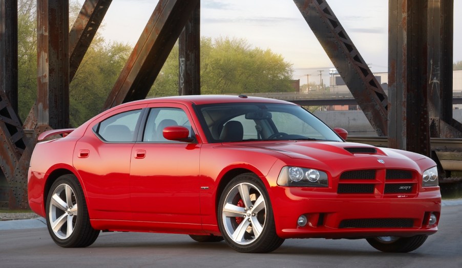 Red 2010 Dodge Charger sedan parked on a bridge, in front of rusted iron uprights.