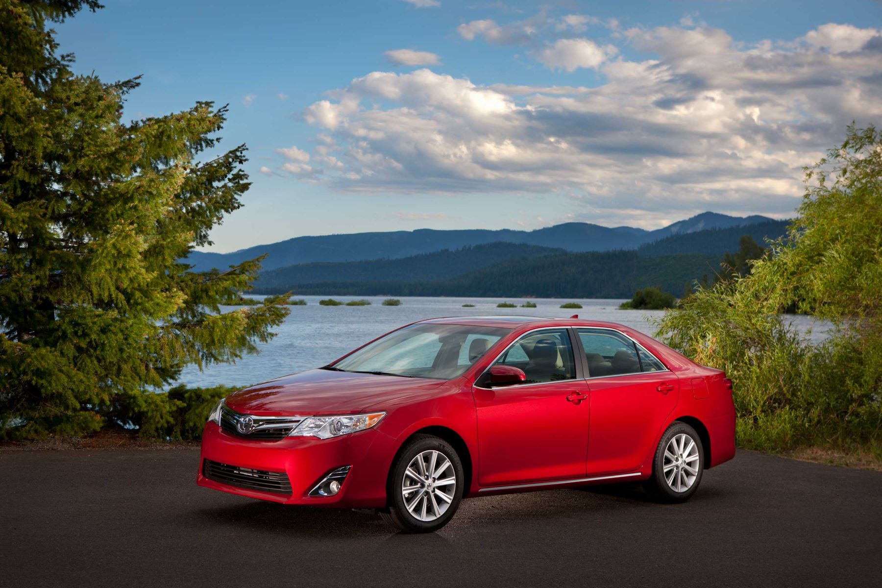 A red 2012-2014 Toyota Camry SE generation midsize sedan model parked near forest trees and the sea