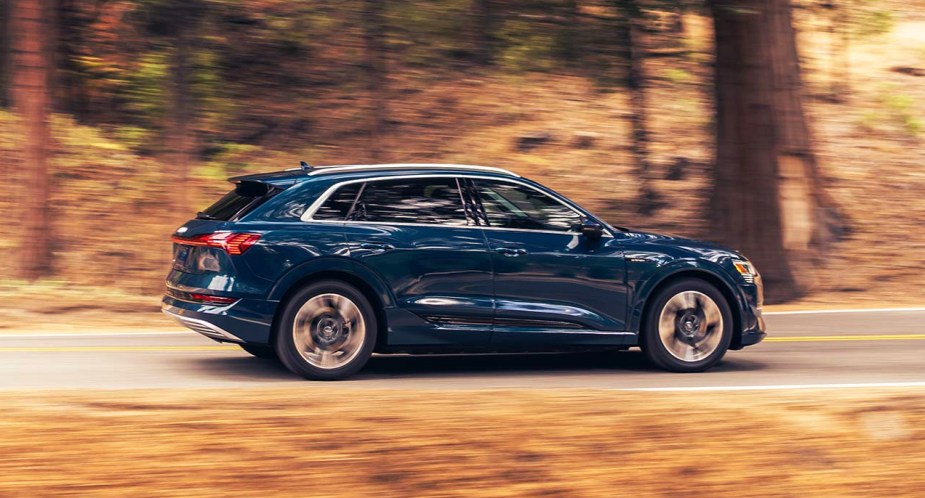 A blue 2023 Audi E-Tron luxury electric midsize SUV is driving on the road. 