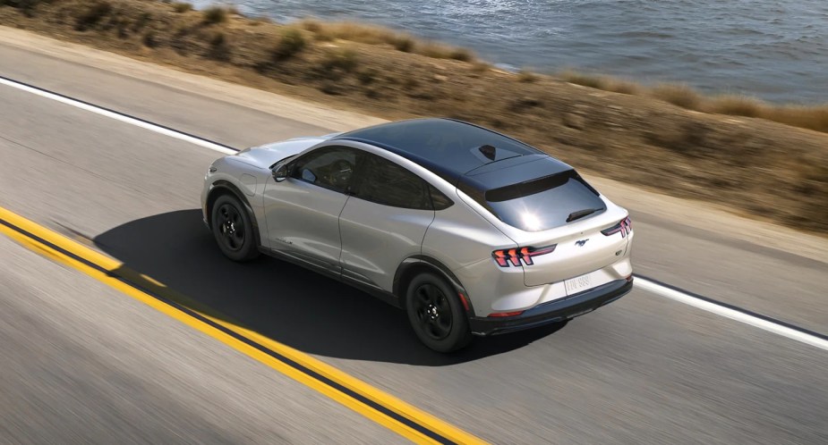 A white 2023 Ford Mustang Mach-E small electric SUV is driving on the road. 