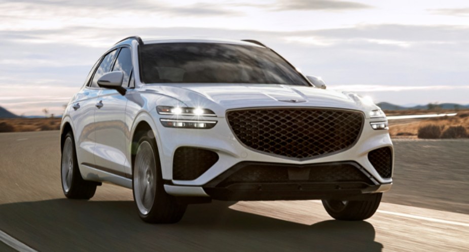 A white 2023 Genesis GV70 small luxury SUV is driving on the road.