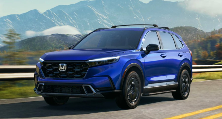 A blue 2023 Honda CR-V LX, the entry level trim, is driving on the road.