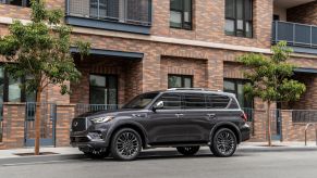 A dark gray 2023 Infiniti QX80 full-size luxury SUV model parked outside a brick apartment building