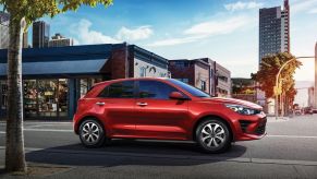 A red 2023 Kia Rio 5-Door hatchback model driving through an urban city