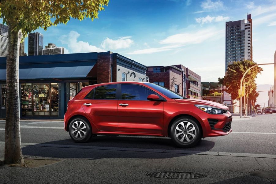 A red 2023 Kia Rio 5-Door hatchback model driving through an urban city