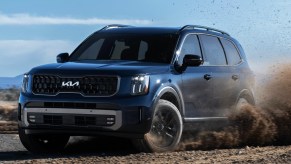 A blue 2023 Kia Telluride midsize SUV is driving off-road.