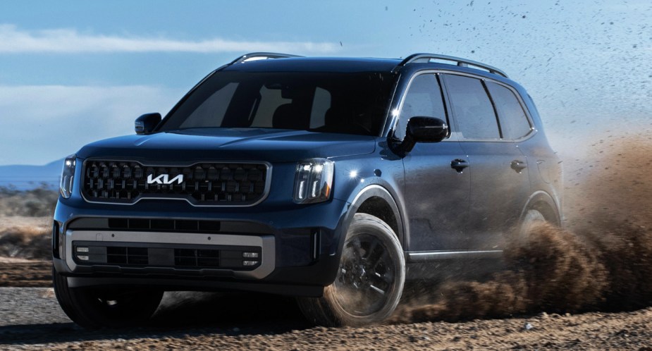 A blue 2023 Kia Telluride midsize SUV is driving off-road. 