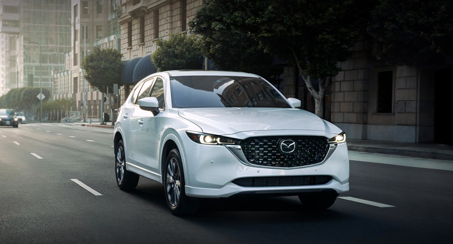 A white 2023 Mazda CX-5 small SUV is driving on the road. 