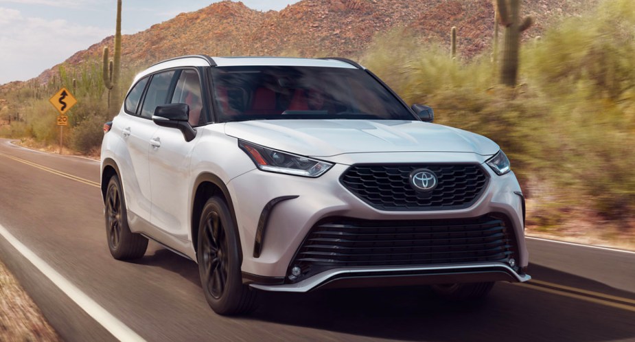 A white 2023 Toyota Highlander midsize SUV is driving on the road. 