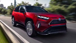 A red 2023 Toyota RAV4 Prime small plug-in hybrid SUV is driving on the road.