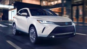 A white 2023 Toyota Venza midsize hybrid SUV is driving on the road.