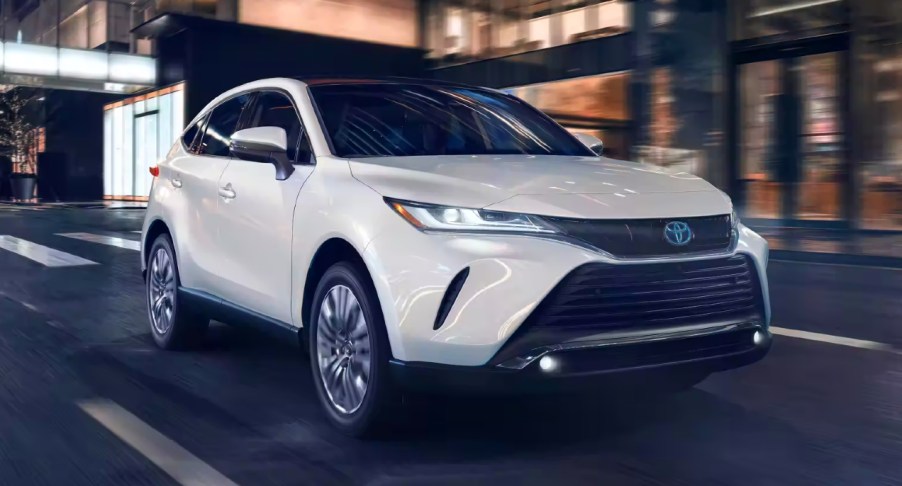 A white 2023 Toyota Venza midsize hybrid SUV is driving on the road.