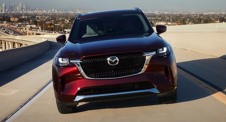 A red 2024 Mazda CX-90 midsize SUV is driving.