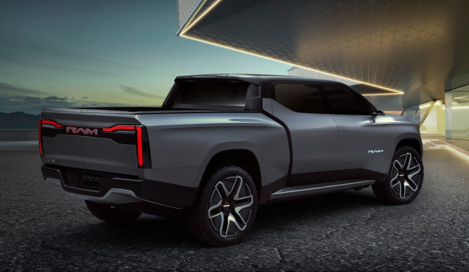 The bed and rear of a Ram Revolution electric concept truck parked on pavement, the sky and a modern house visible in the background.