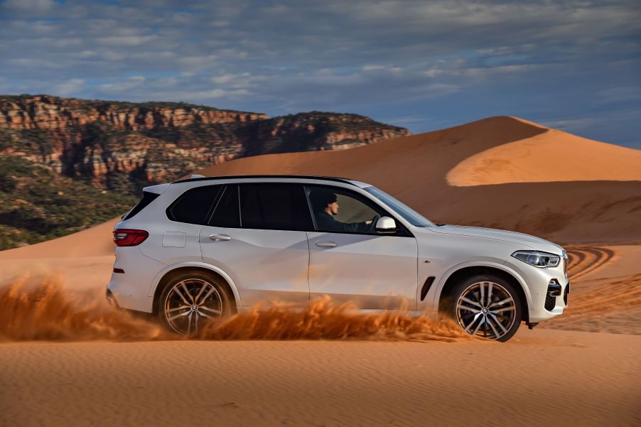 A white A BMW X5 sport activity vehicle (SAV) midsize luxury SUV model driving on sand