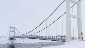 A white car races underneath a snow covered overpass bridge during the winter.