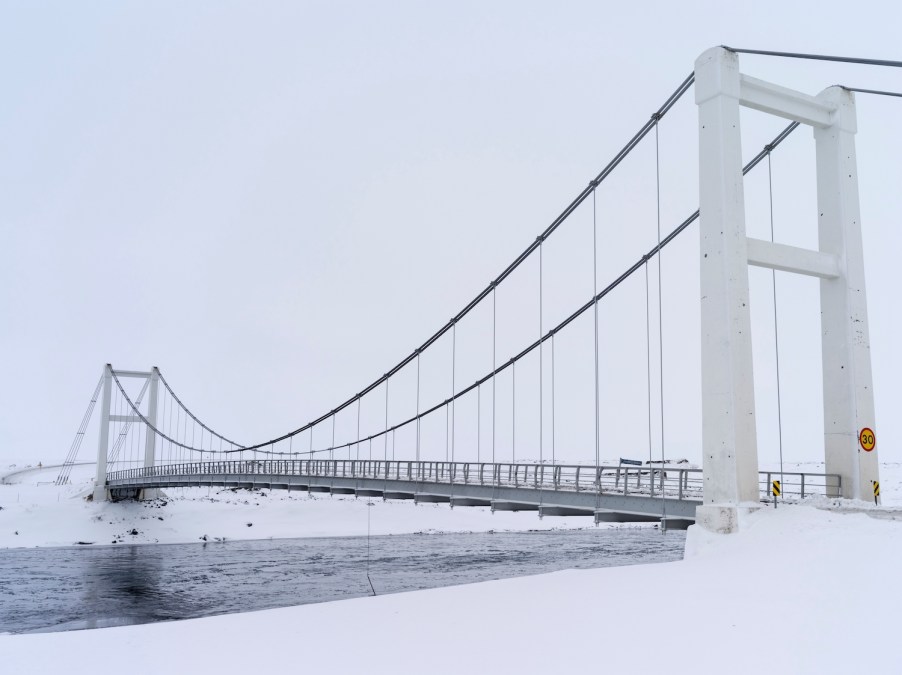 A white car races underneath a snow covered overpass bridge during the winter.