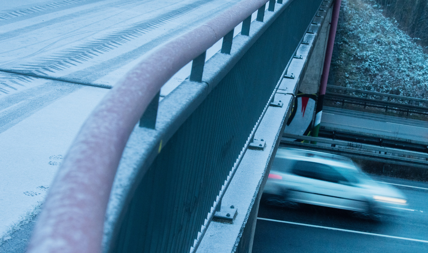 A white car races underneath a snow covered overpass bridge during the winter.