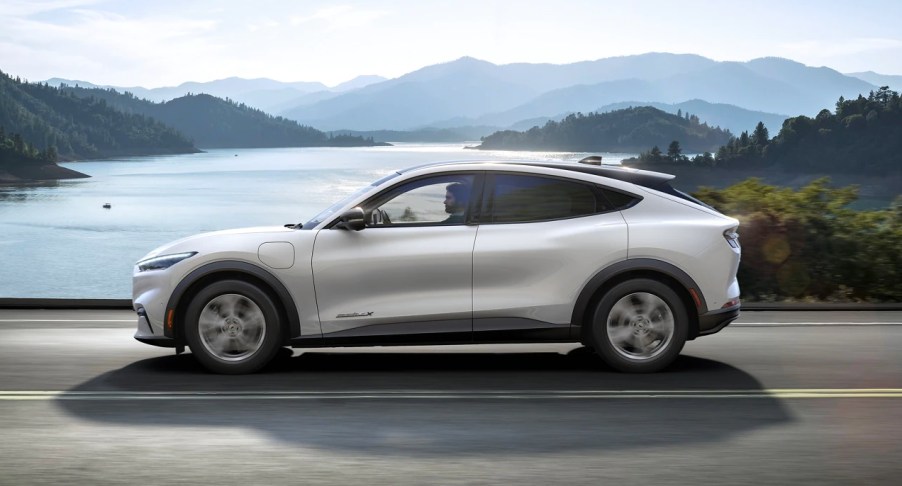 A white 2023 Ford Mustang Mach-E small electric SUV is driving on the road.