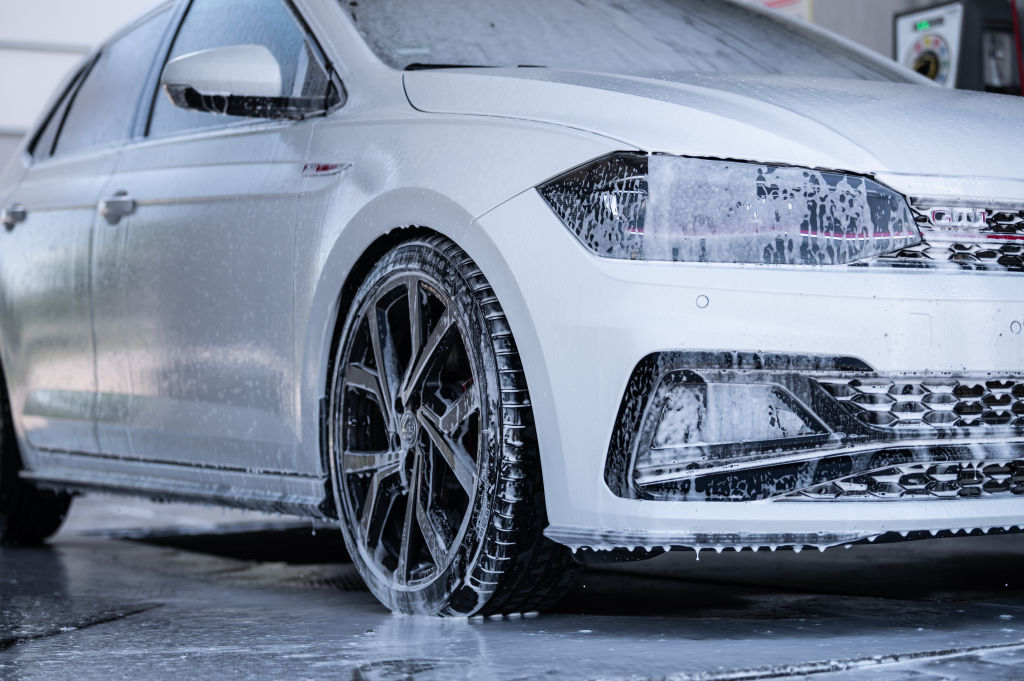 A white car going through a winter car wash, covered in soap and foam.