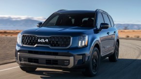 A blue 2023 Kia Telluride midsize SUV is driving on the road.