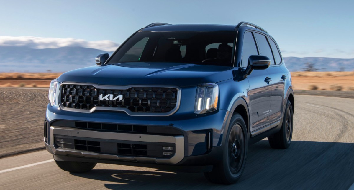 A blue 2023 Kia Telluride midsize SUV is driving on the road.