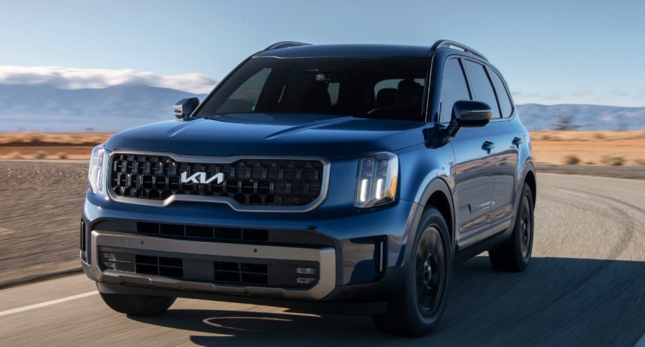 A blue Kia Telluride midsize SUV is driving on the road. 