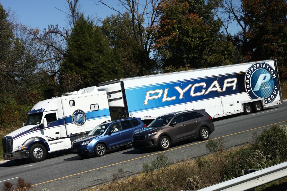 A semi truck braking as it descends a steep hill on the interstate, being passed by cars.