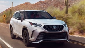 A white 2023 Toyota Highlander midsize SUV is driving on the road.