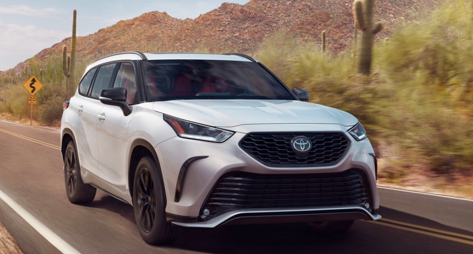 A white 2023 Toyota Highlander midsize SUV is driving on the road.