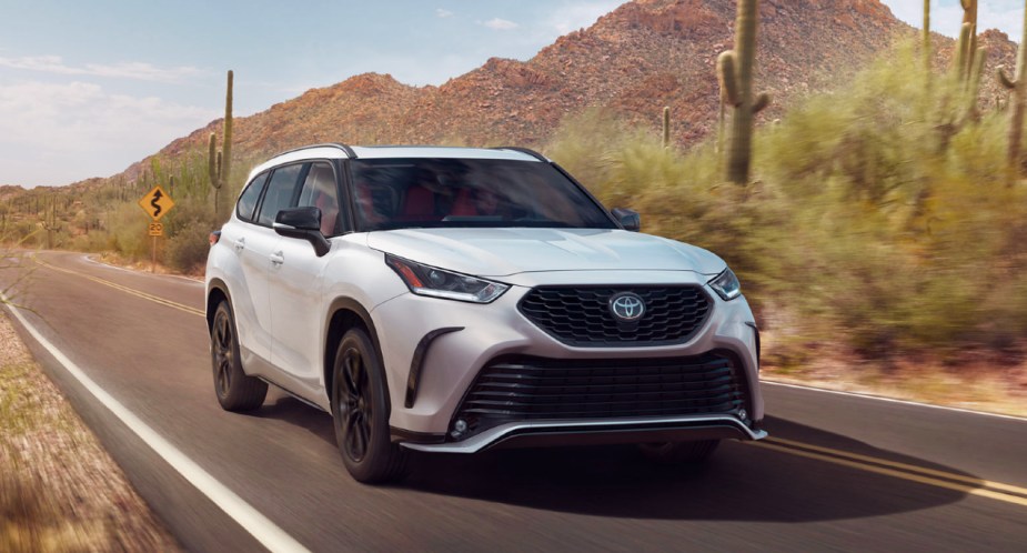 A white 2023 Toyota Highlander midsize SUV is driving on the road. 