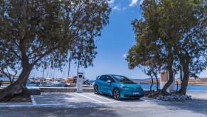 A turquoise Volkswagen ID.4 EV parked in front of the harbor of a greek island.