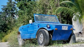 A bright blue Volkswagen Thing off-roader parked in front of a palm tree in Mexico.