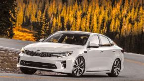 A white 2016 Kia Optima driving down an open road.