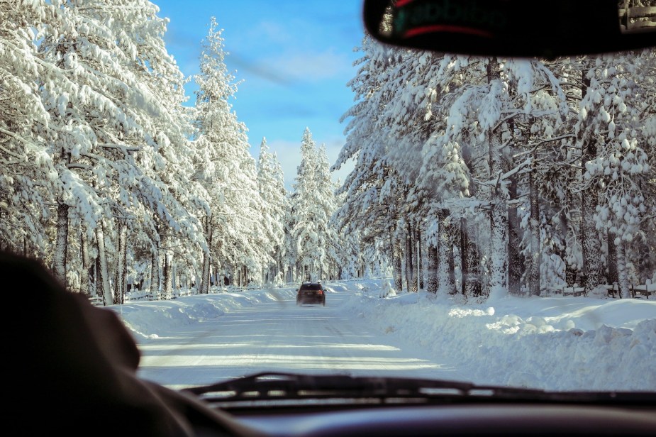 The view of a snowy drive through a car's windshield.