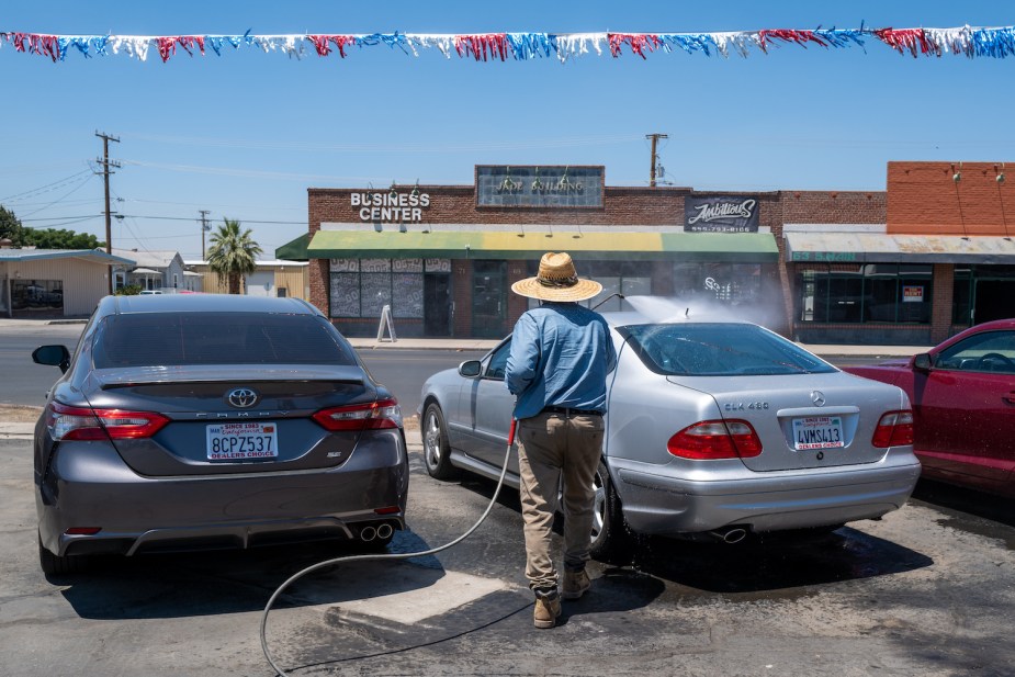 A dealership employee washing a Toyota and Mercedes with custom license plate surround holders installed.