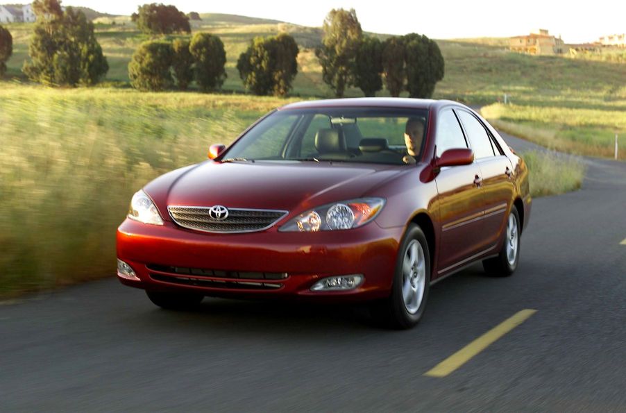 A dark red 2002-2006 Toyota Camry SE midsize sedan model driving past fields of grass