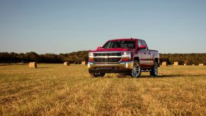 A red 2016 Chevrolet Chevy Silverado 1500 LT full-size pickup truck model parked on a farm hay field