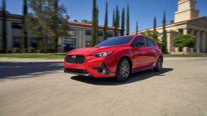 A red 2024 Subaru Impreza RS compact car model driving past a building with marble columns