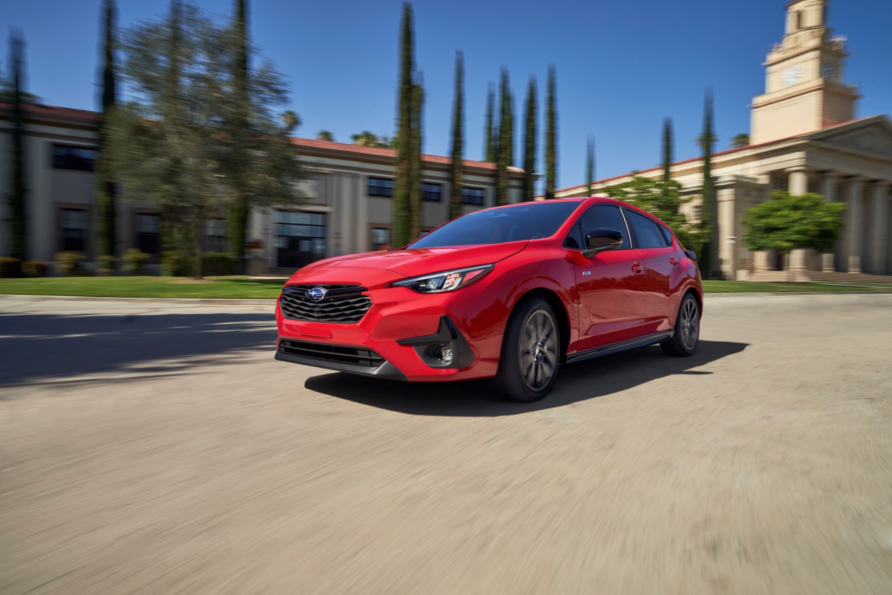 A red 2024 Subaru Impreza RS compact car model driving past a building with marble columns