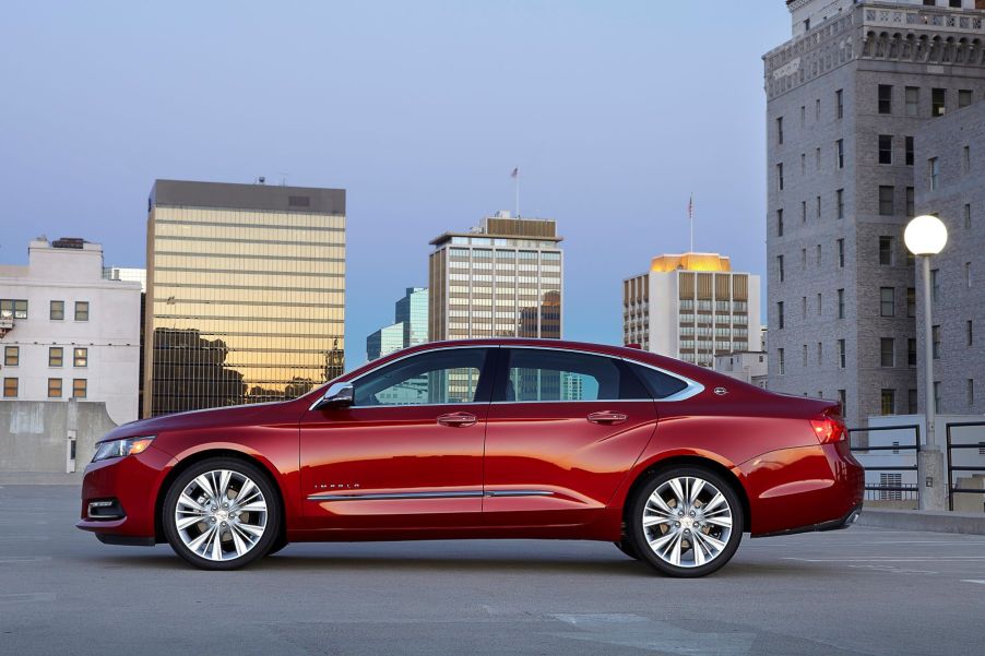 A side profile of a red 2018 Chevrolet Chevy Imapala full-size sedan model parked on the top of a parking garage