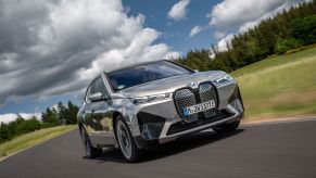 A silver-gray BMW iX M60 all-electric luxury SUV model driving under darkening clouds