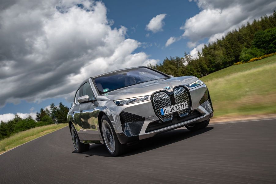 A silver-gray BMW iX M60 all-electric luxury SUV model driving under darkening clouds